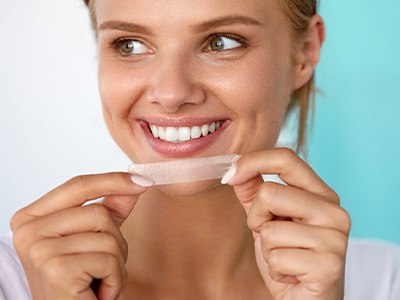 Woman smiling while holding whitening strip
