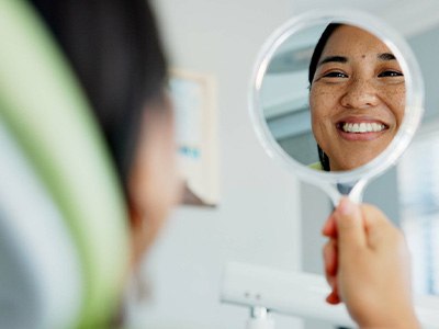 Woman smiling at reflection in handheld mirror