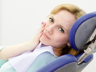 Woman holding her cheek in pain while in dental chair