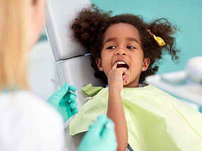 Young girl in dental chair pointing to her tooth