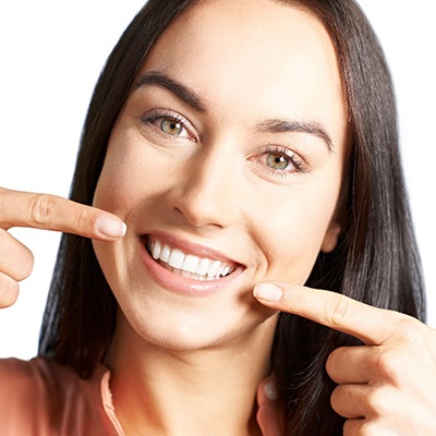Woman pointing to her teeth after correcting them with Invisalign. 