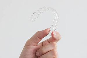 Nearly invisible Invisalign aligner being held aloft