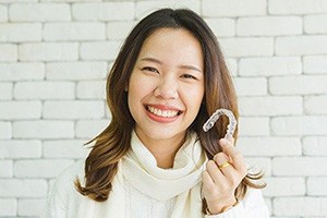 Woman with a beautiful smile holding an Invisalign aligner