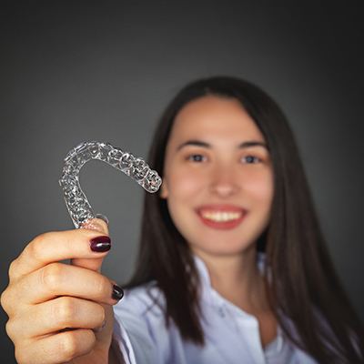 Woman smiling and holding an Invisalign aligner out in front of her