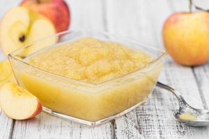 a bowl of applesauce on a table with apples