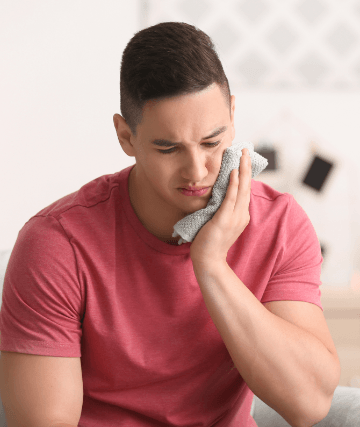 Young man in pain holding cold compress to his cheek