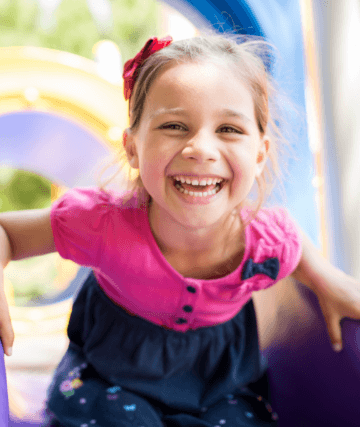 Young girl in pink laughing on playground