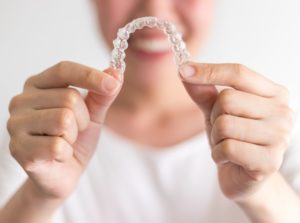 Smiling woman holding Invisalign aligner out in front of her