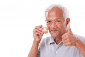 Senior man holding dentures and giving a thumbs up. 